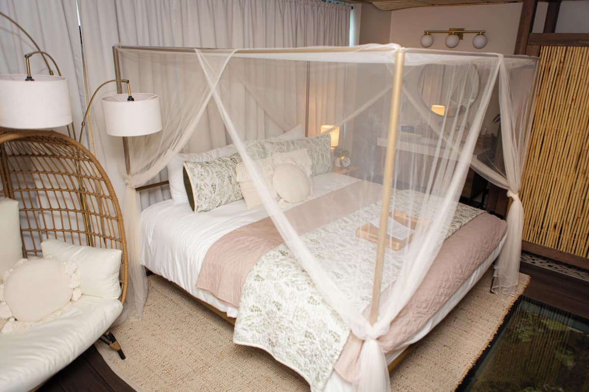 Una cama con dosel, una lámpara de noche y una silla de mimbre.