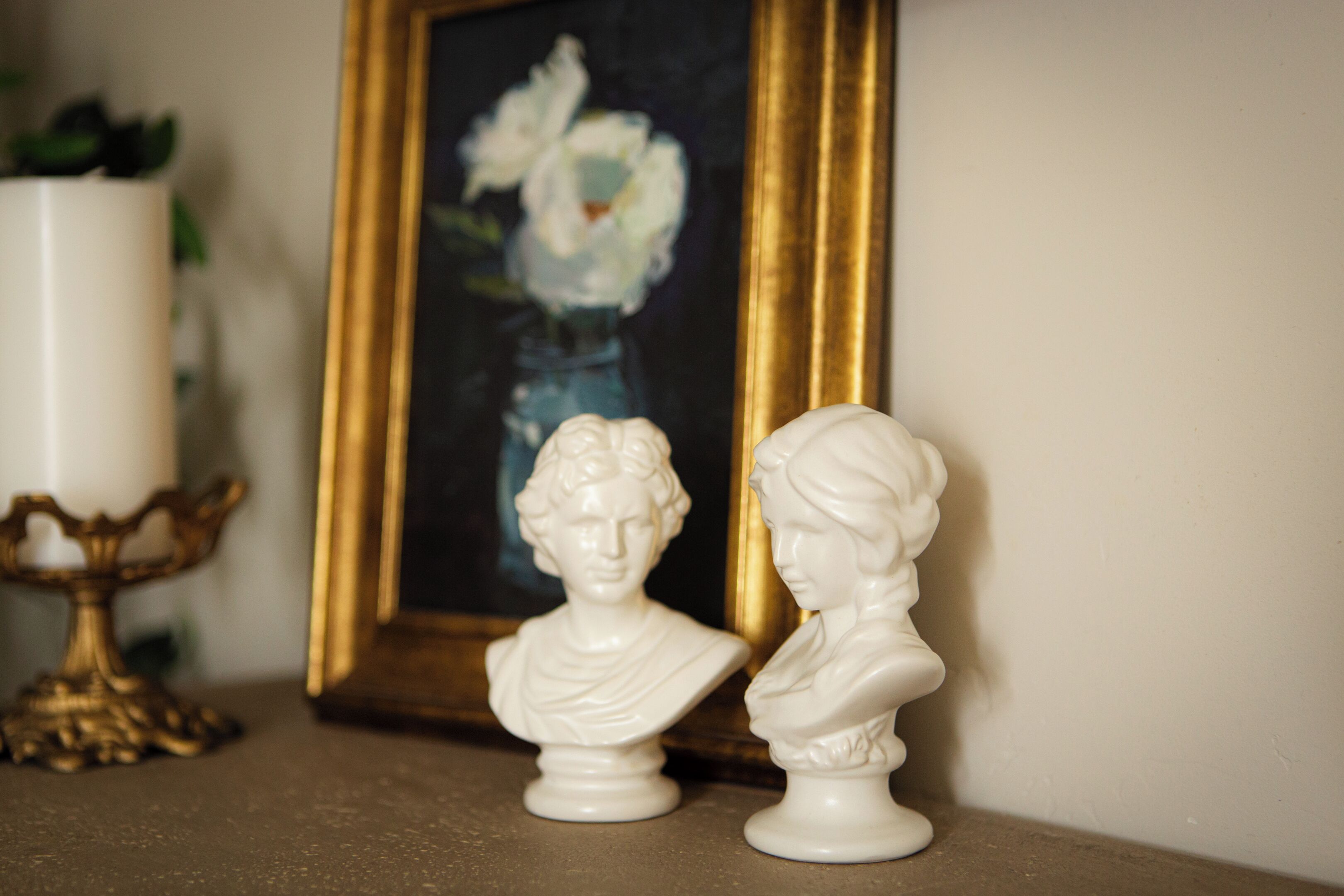 Un busto sobre una mesa, un cuadro enmarco y un candelabro.