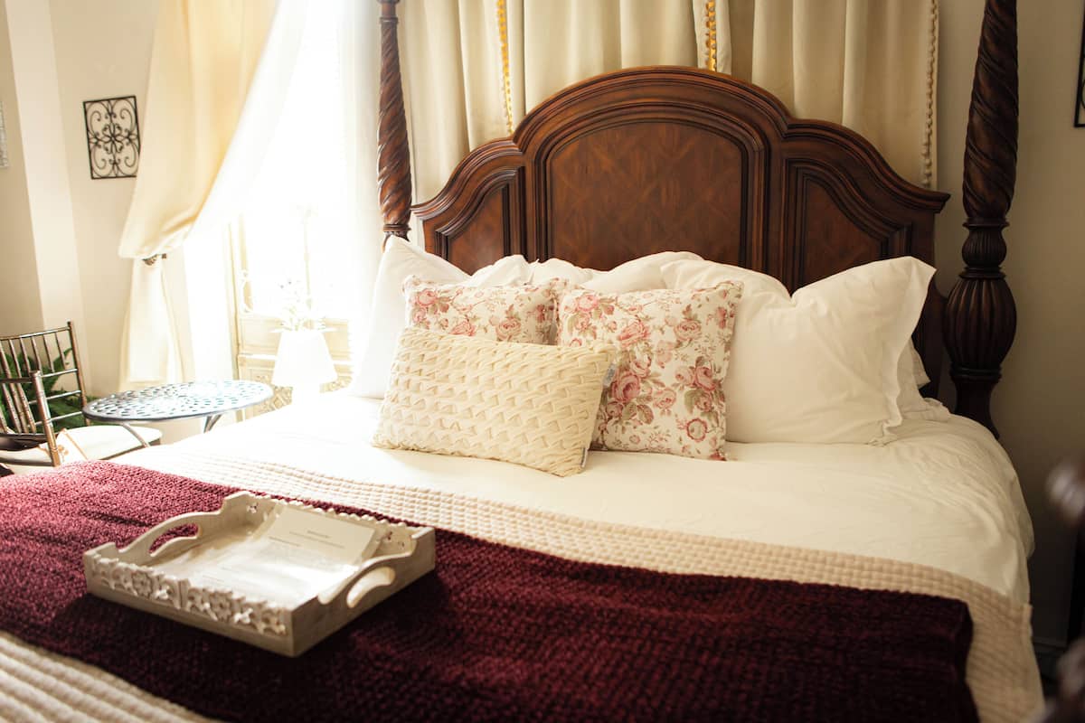 Una cama bien hecha con cabecera de madera, manta roja y almohadillas estampadas con flores.