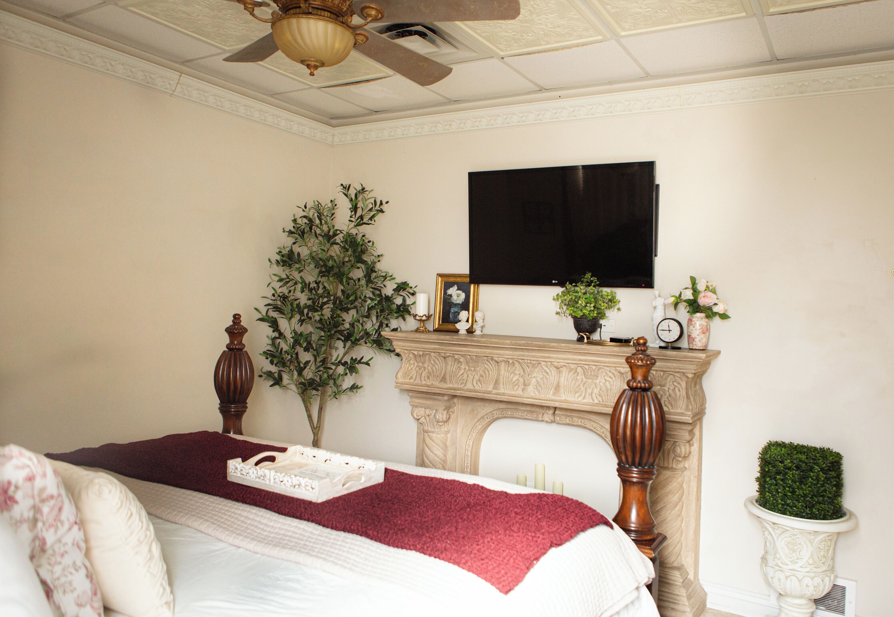 A bedroom with a bed, a ceiling fan, a fireplace, and a television mounted on the wall.