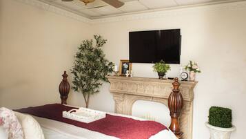 A bedroom with a bed, a ceiling fan, a fireplace, and a television mounted on the wall.