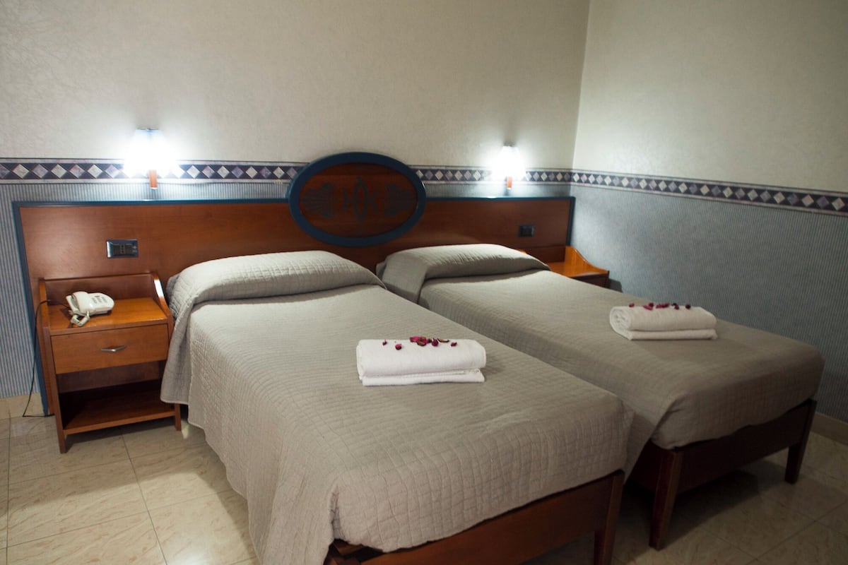 A hotel room with two beds, a nightstand with a phone, and a wall-mounted light fixture.
