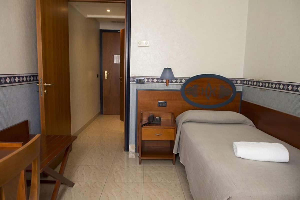 A hotel room with a bed, a wooden nightstand, a desk, and a chair.