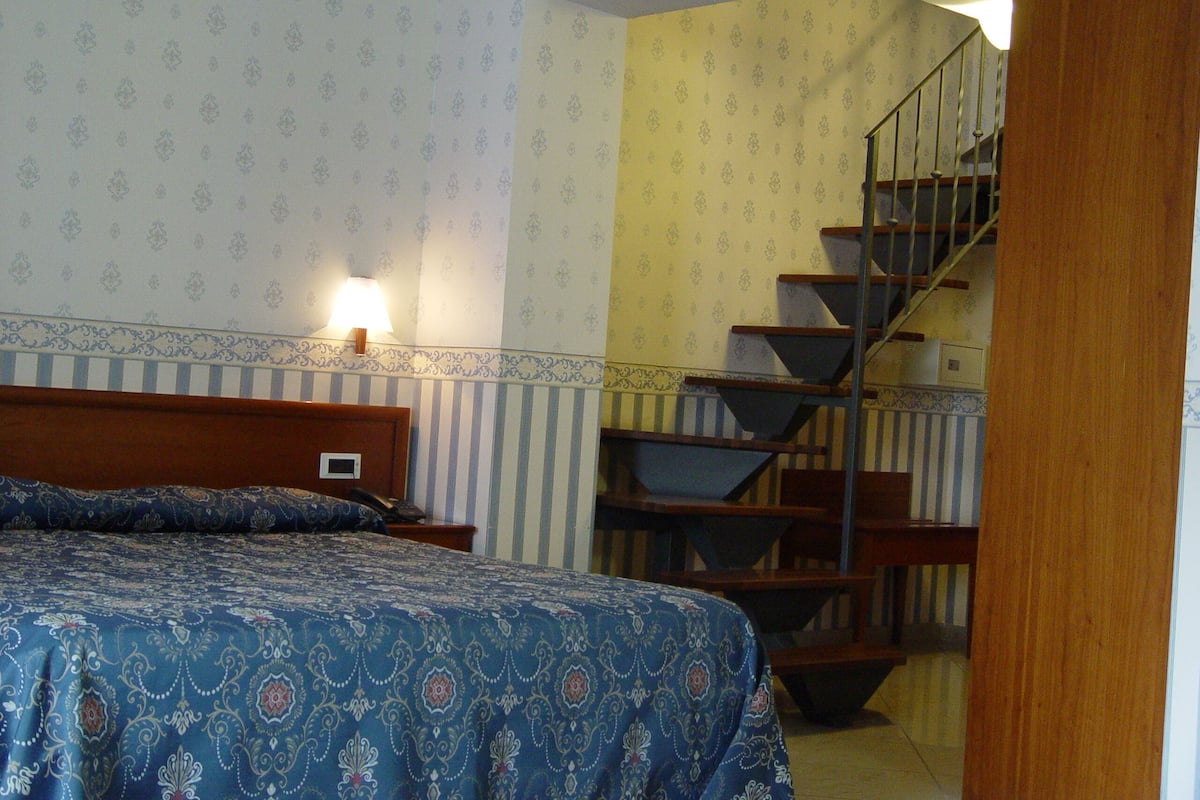A bedroom with a bed, a nightstand, a lamp, and a staircase.