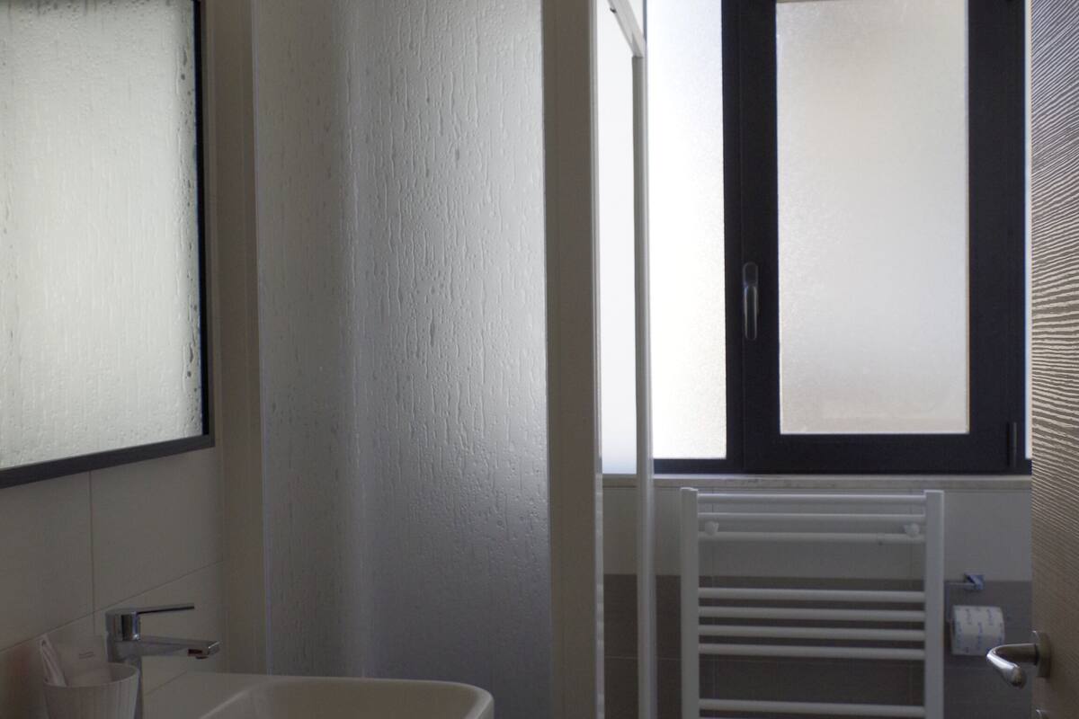 A bathroom with a white sink, a mirror, a window with blinds, and a white radiator.