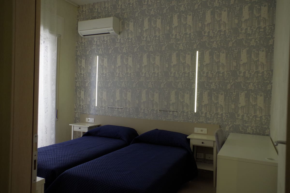A bedroom with two beds, a small desk, and a white wardrobe.