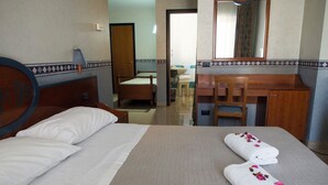 A hotel room with two beds, a wooden headboard, a bathroom with a mirror, and a desk with a chair. - Hotel Kroma (Ragusa)