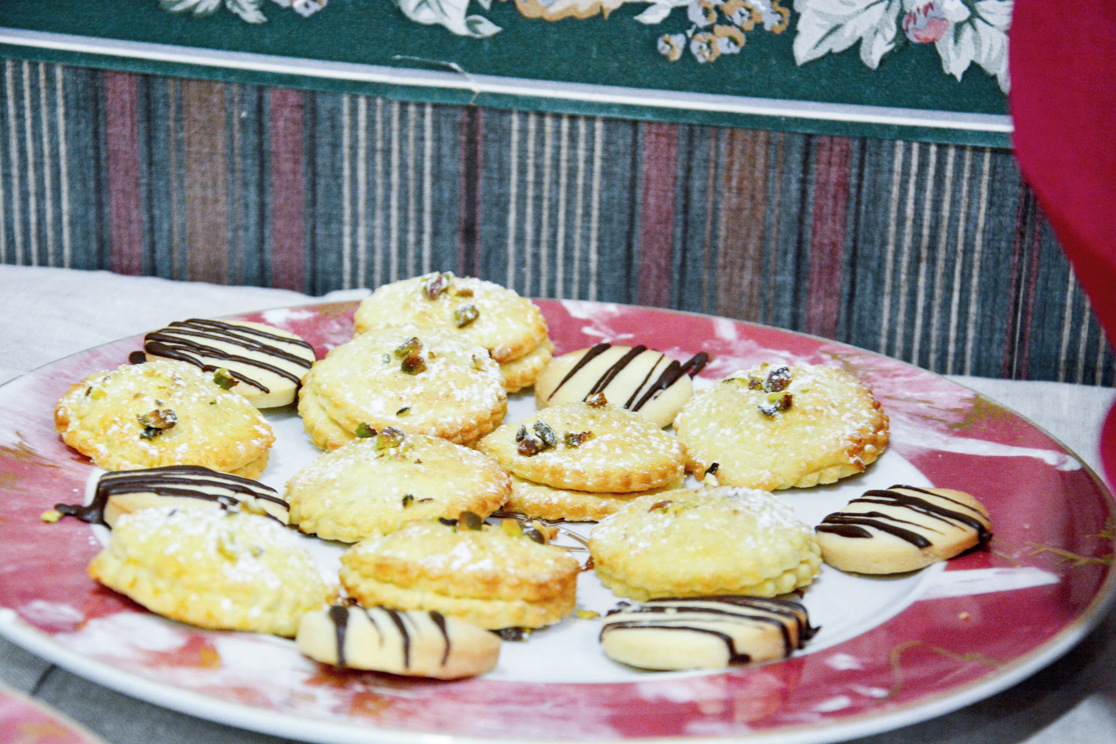 A plate of assorted cookies with chocolate drizzle and nuts, placed on a floral-patterned plate.