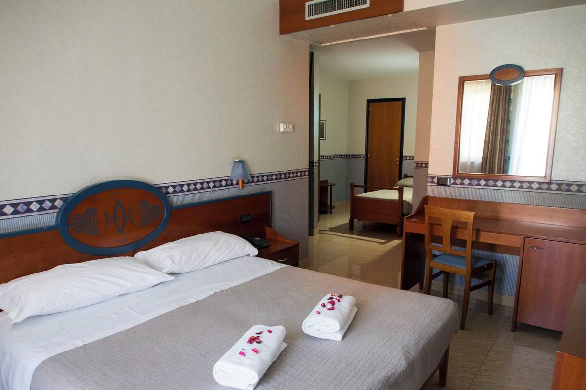 A hotel room with a bed, a desk, a chair, and a mirror.