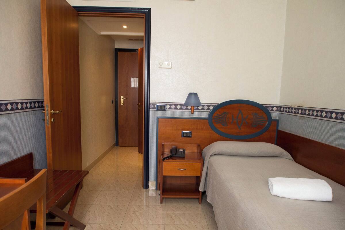 A hotel room with a bed, a nightstand, a desk, and a chair.
