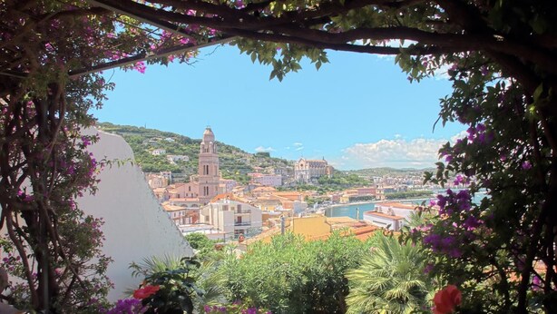 Une vue d’une ville côtière, avec une tour imposante, une végétation luxuriante et un ciel dégagé.