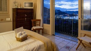 Une chambre d’hôtel comprenant un lit, une télévision, une armoire en bois, une chaise et un balcon avec vue sur la ville.