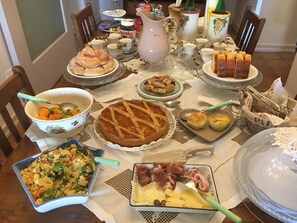 Une table à manger dressée avec différents plats, notamment une tarte, une salade et un plateau de fromages.