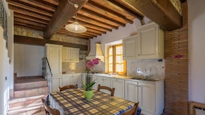 A kitchen with white cabinets, a dining table with a checkered tablecloth, and a staircase leading to another level. - Agriturismo Tontenano (Bucine)