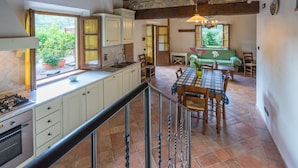 A kitchen with white cabinets, a gas stove, and a dining area with a table and chairs. - Agriturismo Tontenano (Bucine)