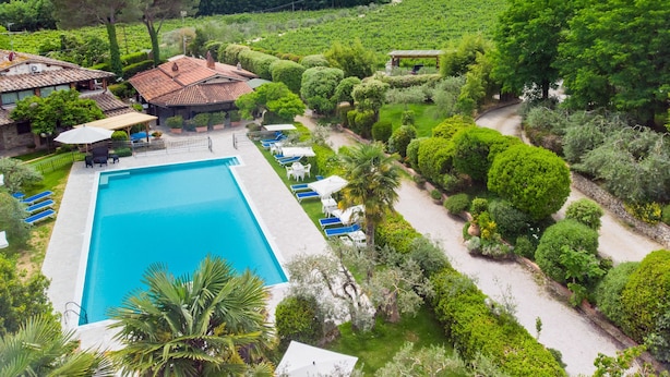 A pool area with lounge chairs and a pergola, surrounded by well-manicured gardens and a vineyard in the background. - Agriturismo Tontenano (Bucine)