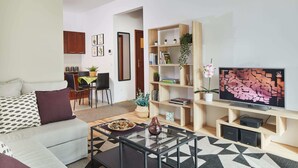 Een moderne woonkamer met een bank, salontafel, televisie, boekenkast en een eethoek met stoelen en een tafel.