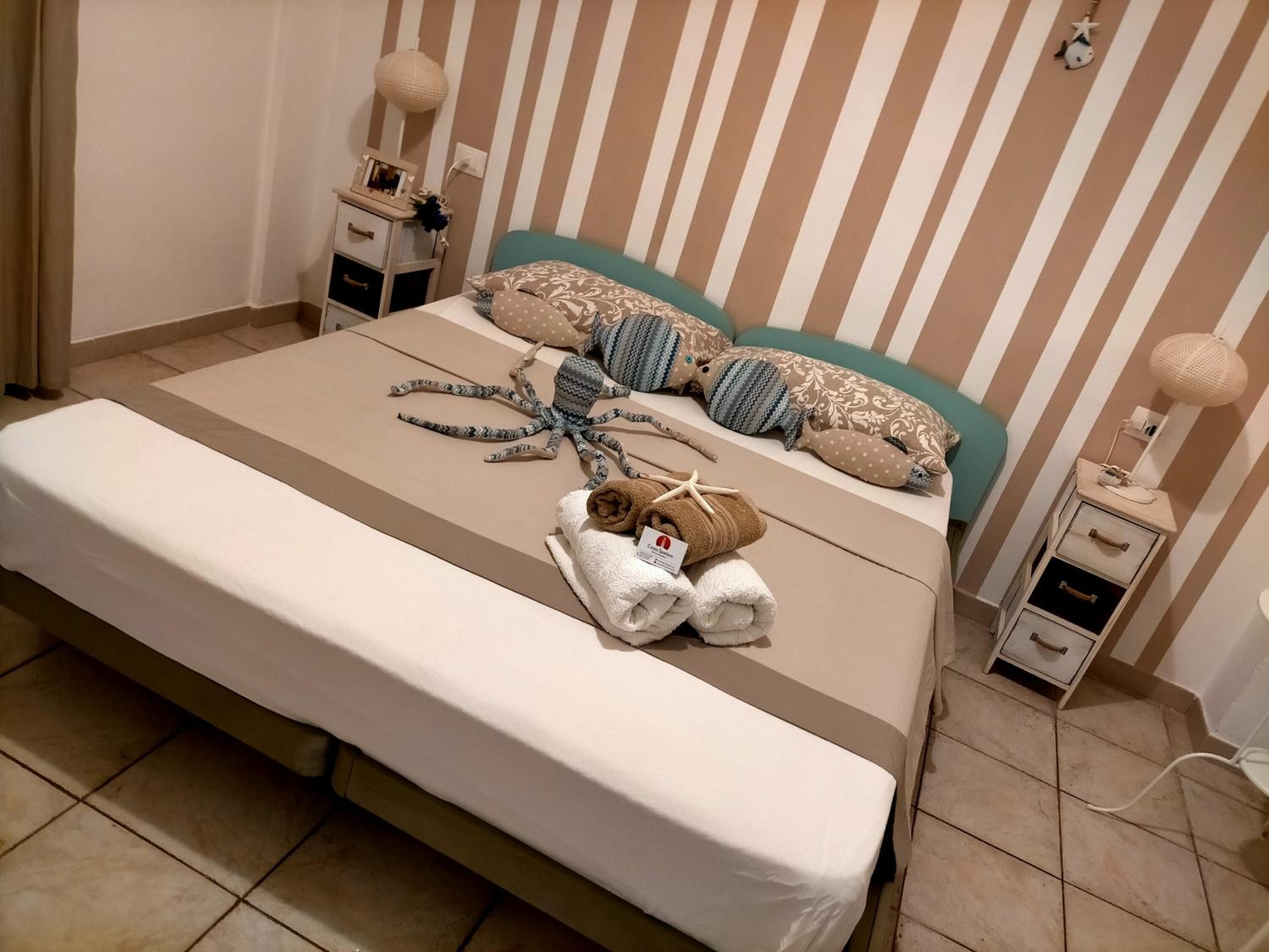 A neatly made bed with striped bedding, a small bedside table with a lamp, and a wall-mounted outlet.