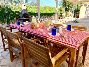 An outdoor dining area with a checkered tablecloth, wooden chairs, and a barbecue grill. - Cozzo Spadaro B&B (Pachino)