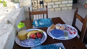 A table set for breakfast with plates of fruit, bread, and pastries, a glass of juice, and a bottle of water. - Cozzo Spadaro B&B (Pachino)