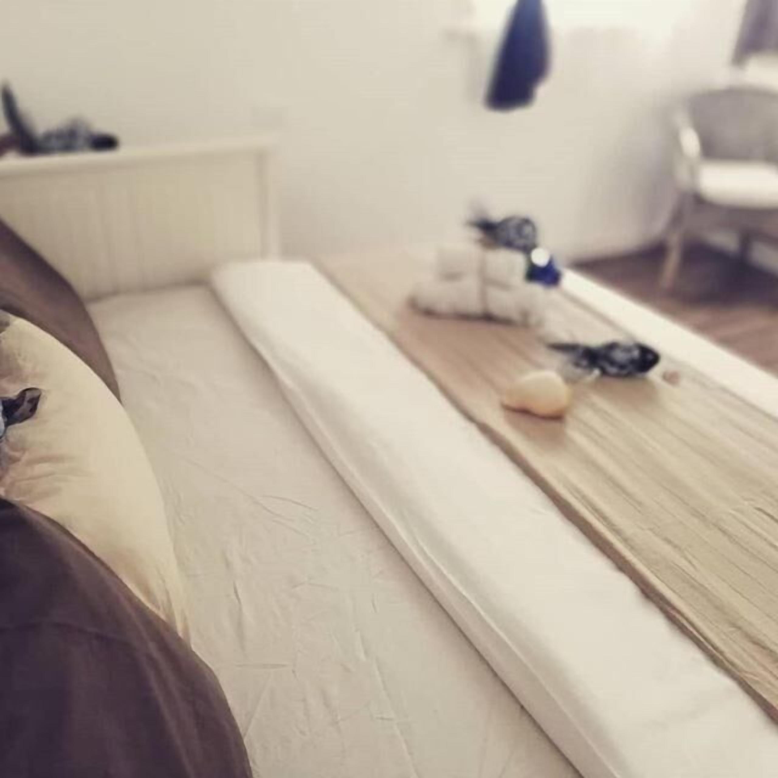 Una cama con colchón blanco y cabecera de madera. Hay una mesita con un objeto azul encima.