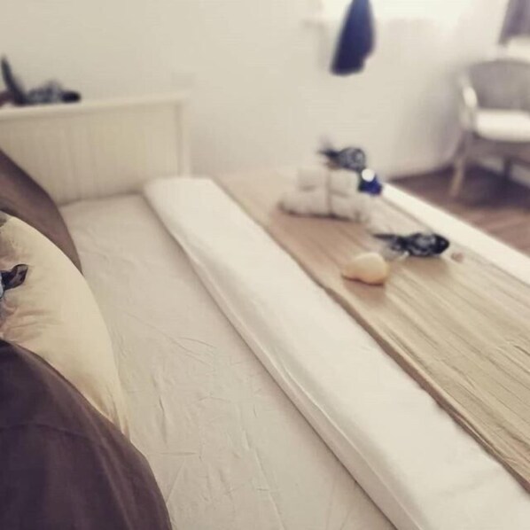 Una cama con colchón blanco y cabecera de madera. Hay una mesita con un objeto azul encima.