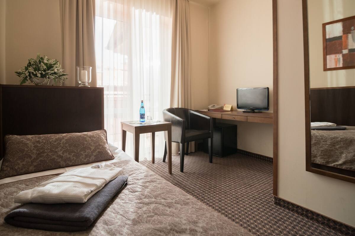 Habitación de hotel con cama, escritorio, silla, computadora y espejo.
