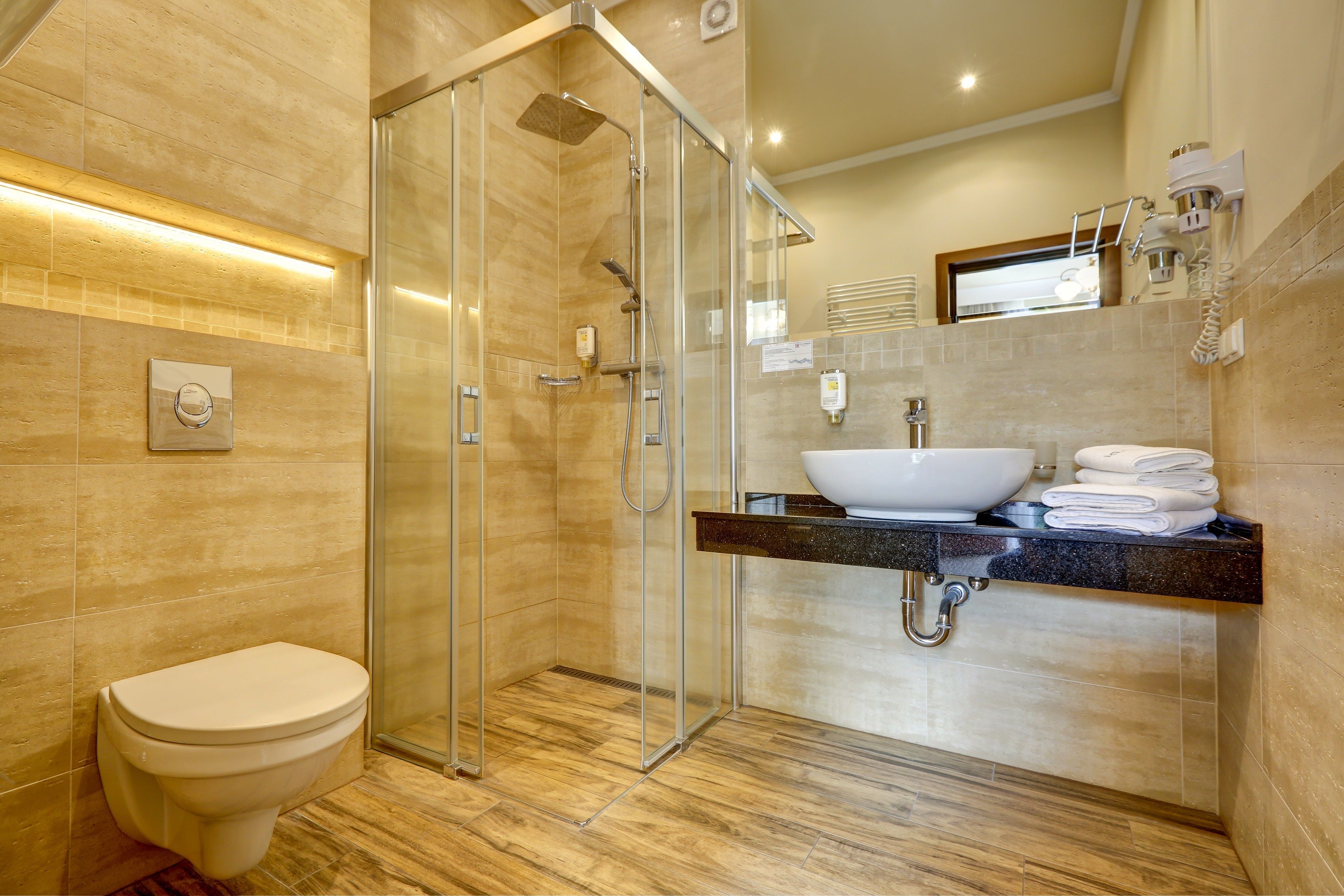 A modern bathroom with a glass-enclosed shower, a white toilet, and a vanity with a sink and towel rack.