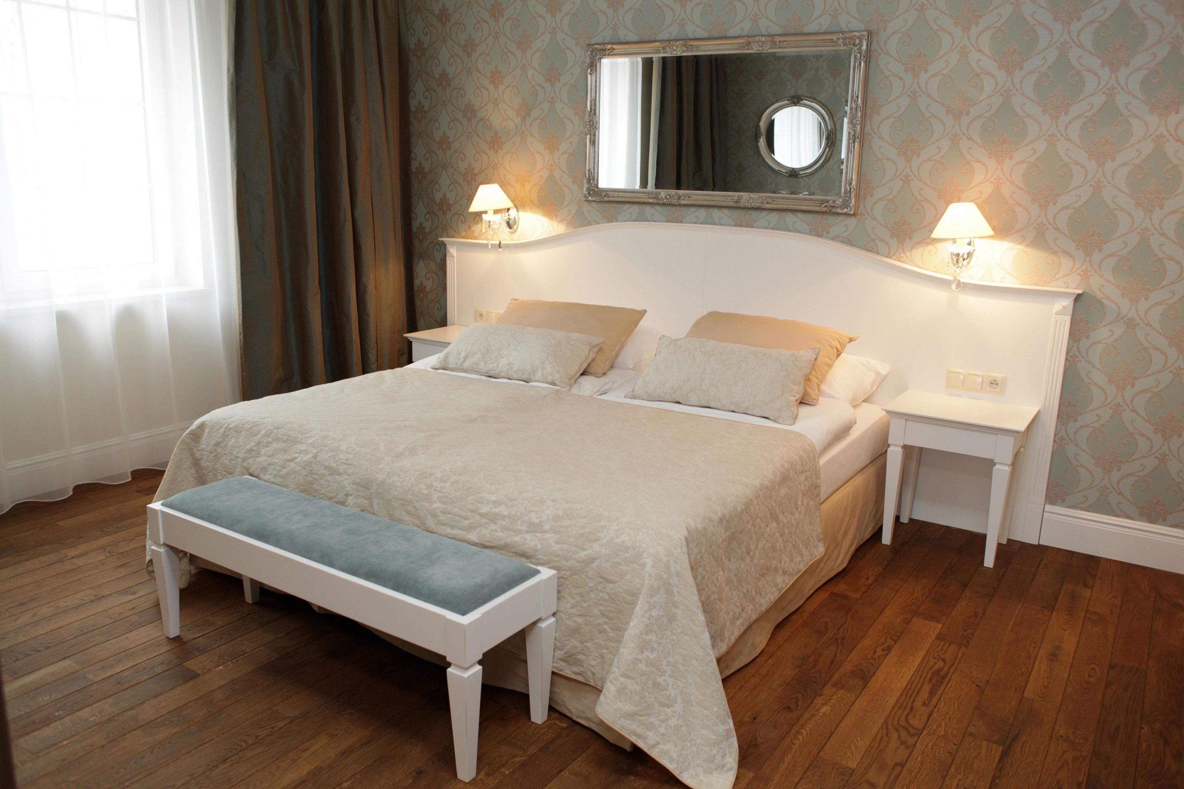 A neatly arranged bedroom with a large bed, bedside tables, a bench, and a mirror on the wall.