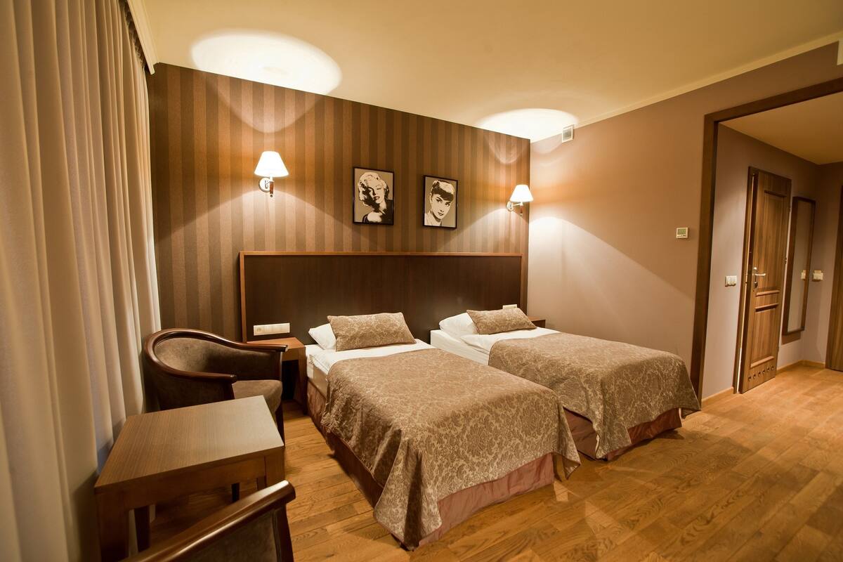 Habitación de hotel con dos camas, un escritorio, una silla y dos lámparas de pared.