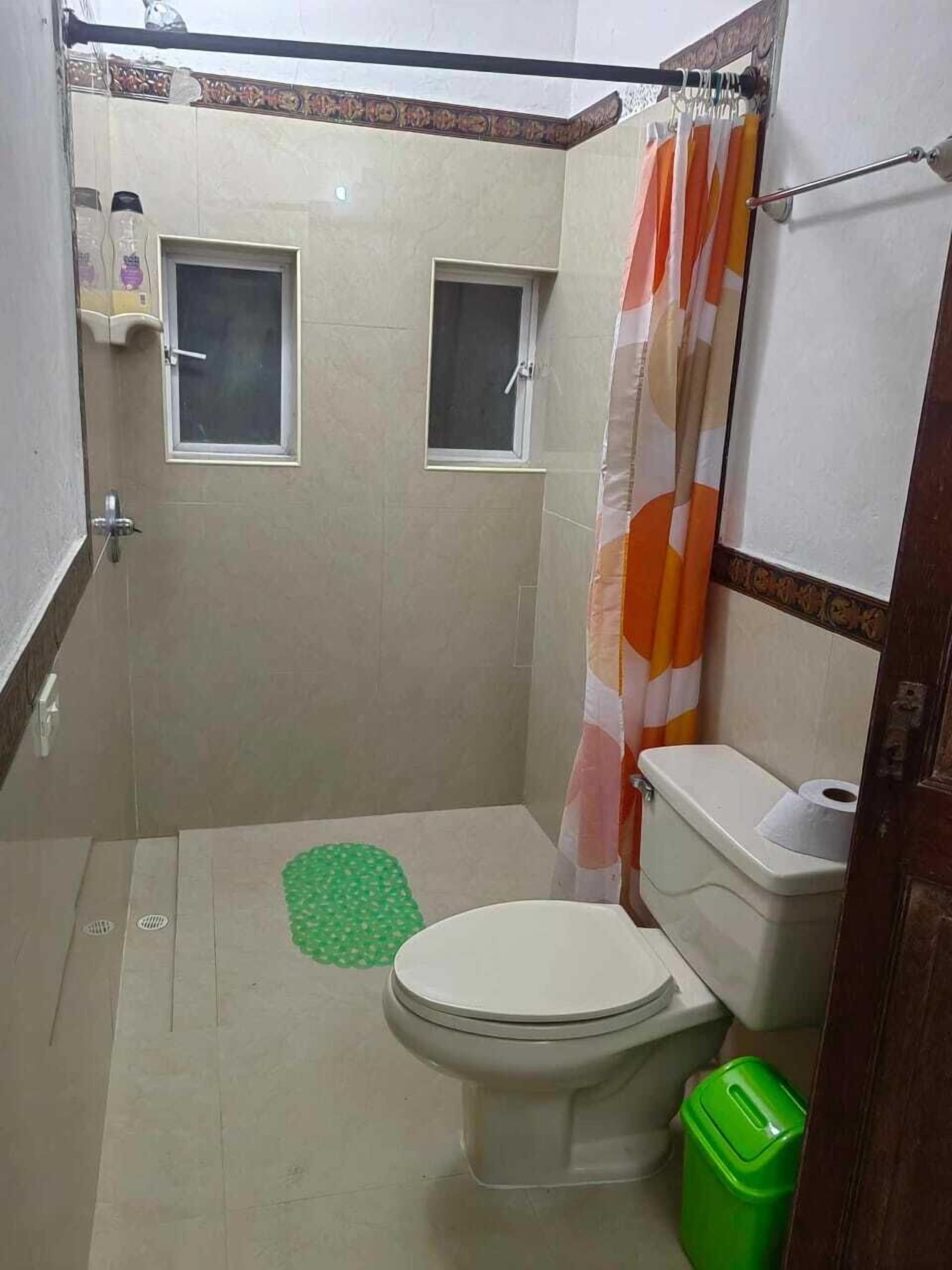 Un baño pequeño con un inodoro, un bote de basura verde y una cortina de ducha.