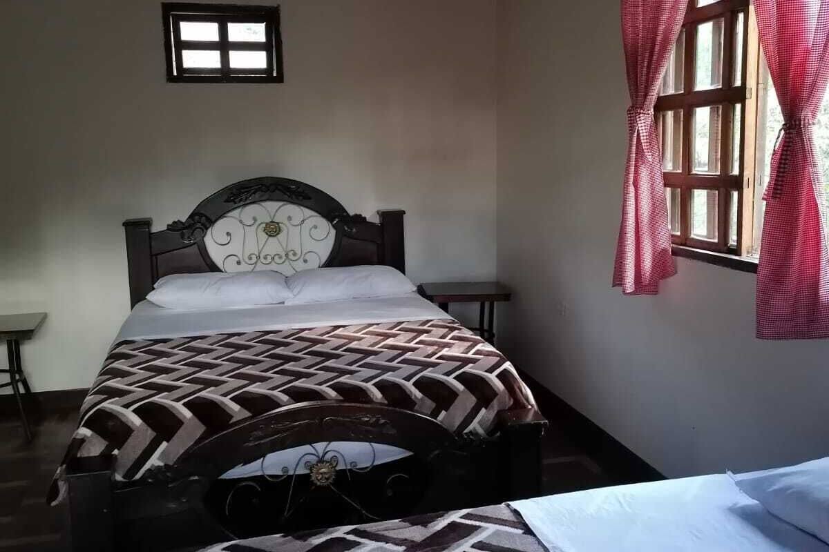 A bedroom with a bed, a window with curtains, a small table, and a wall-mounted shelf.