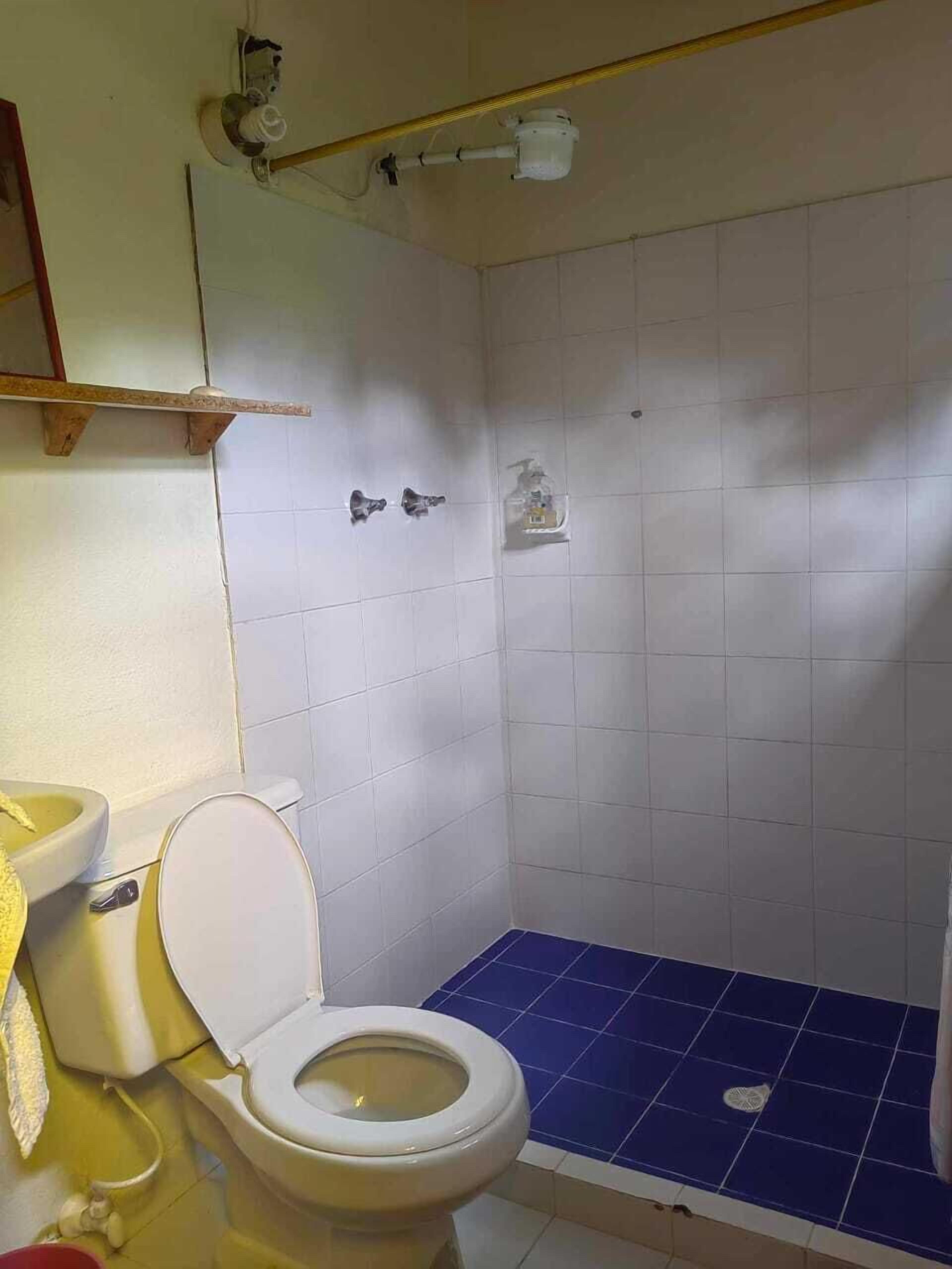 Un baño con inodoro, piso de ducha azul y lavamanos blanco.