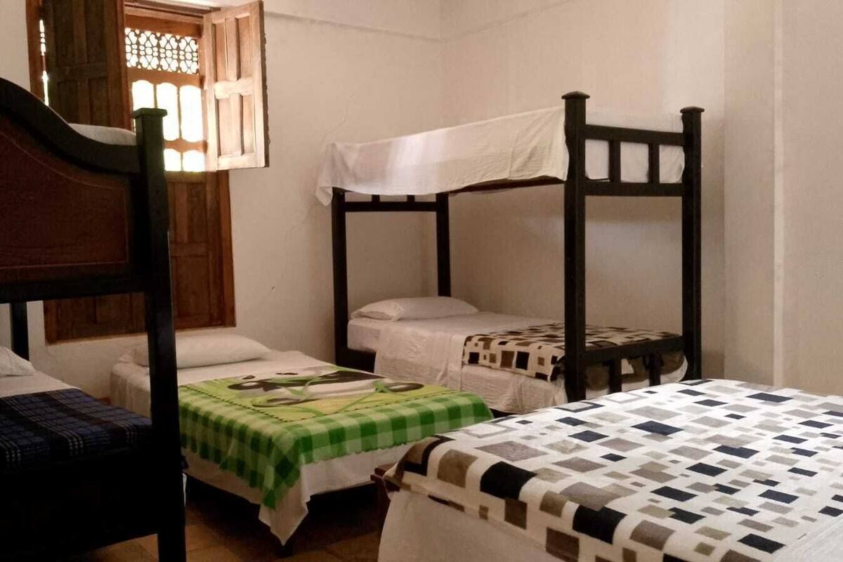 A dormitory room with three bunk beds, a window with a wooden frame, and a white wall.
