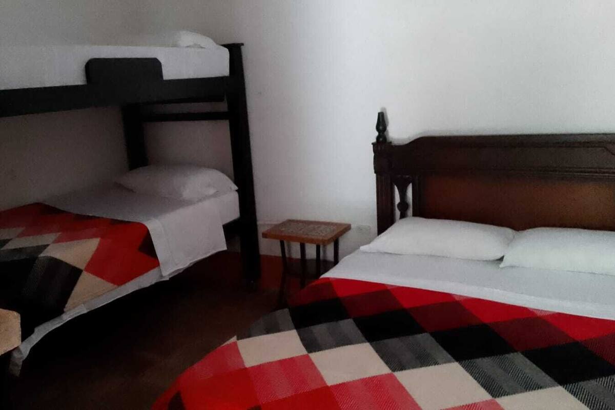 A room with two bunk beds, a small wooden table, and a bed with a checkered blanket.