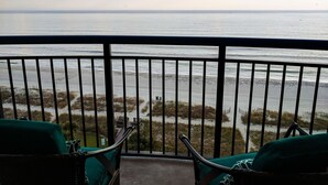 A balcony with two green cushioned chairs facing a beach. - Boardwalk 932 (Myrtle Beach)