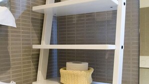 A bathroom with a white shelf unit holding a basket, a jar of cotton swabs, and a vase with white flowers. - B&B Casetta Roma  (Rome)