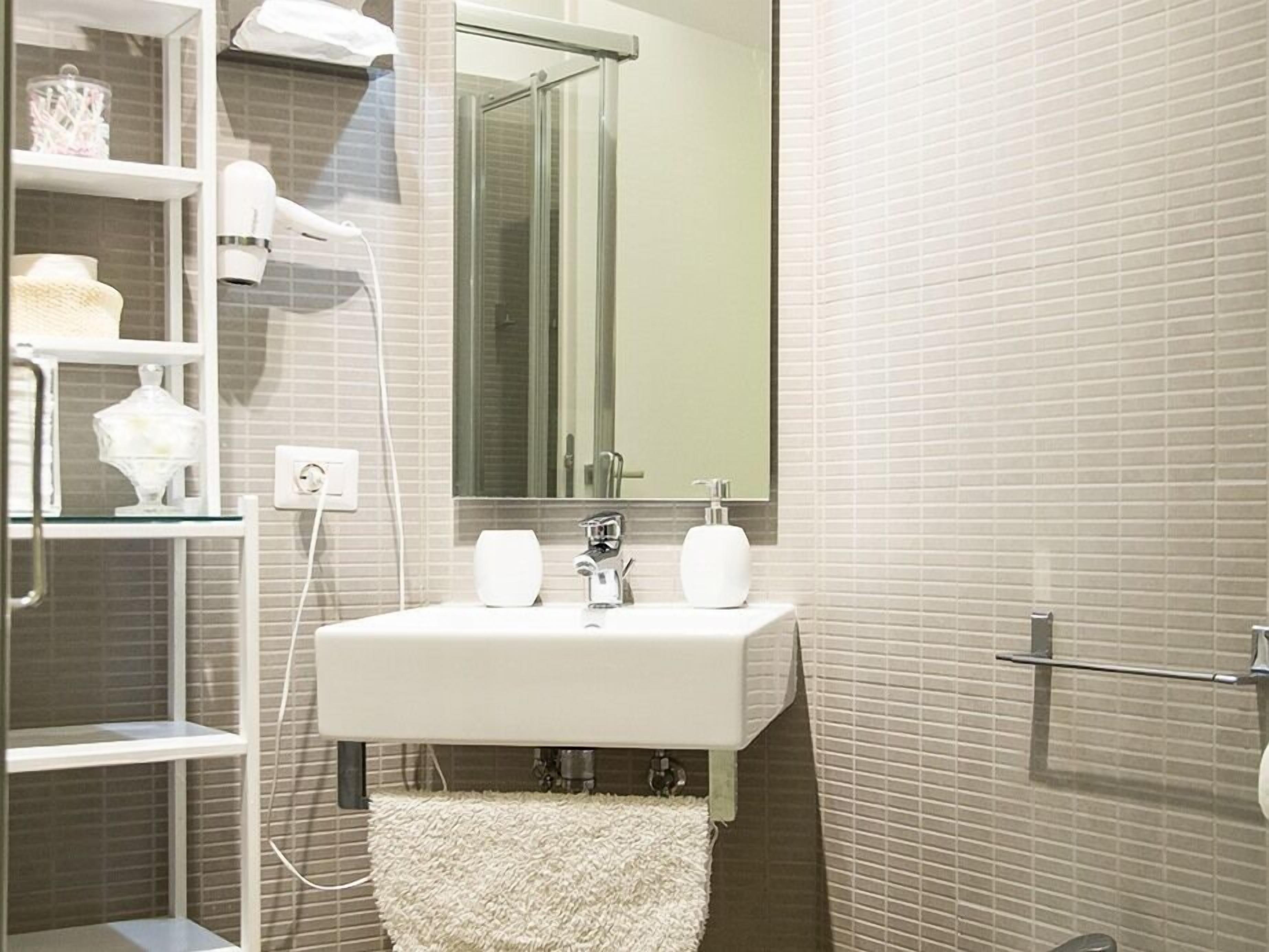 Un baño con un lavamanos blanco, un espejo y una cabina de ducha de vidrio.