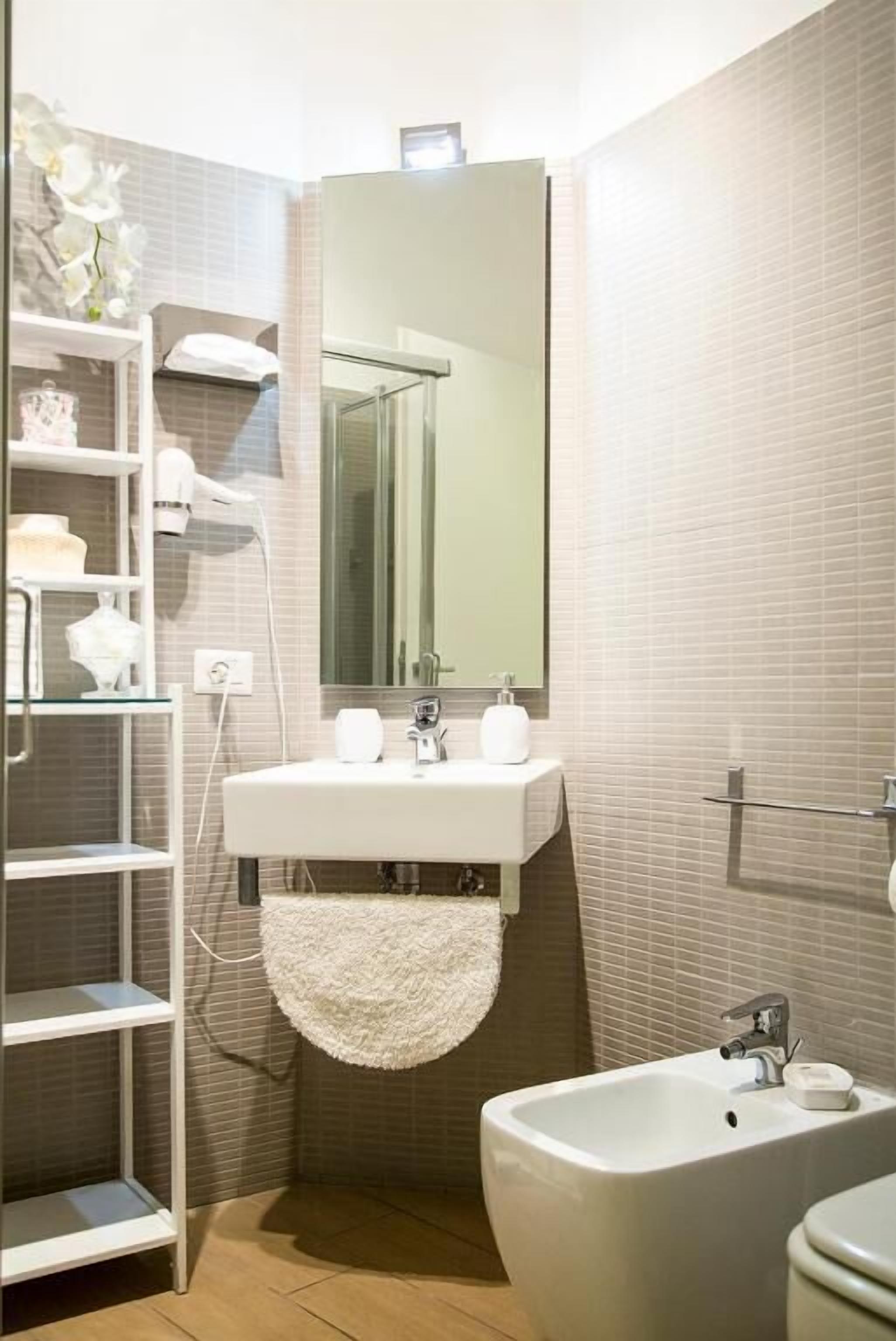 A bathroom with a white sink, a mirror, a bidet, and a towel rack.