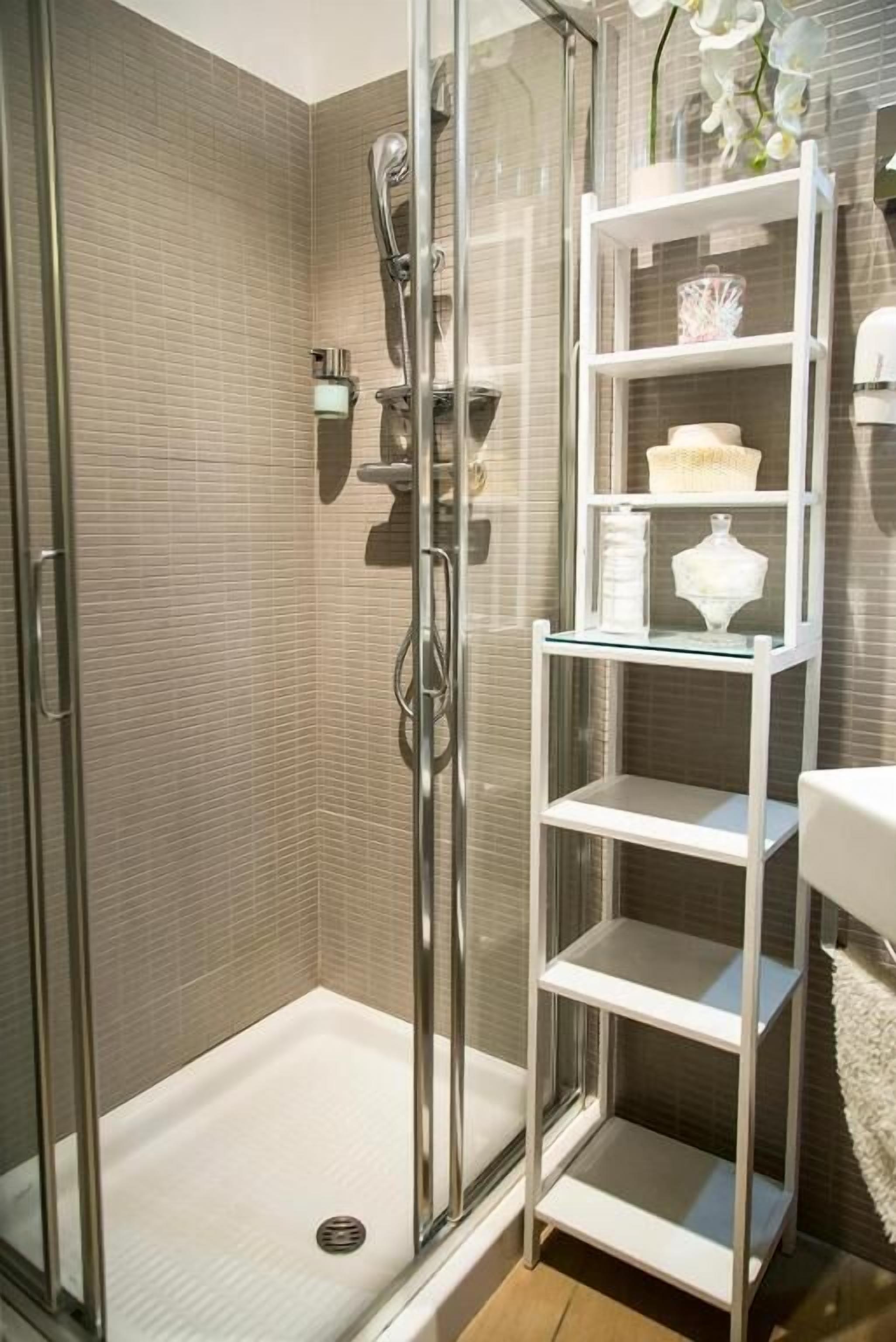Ein modernes Badezimmer mit einer in Glas abgeschlossenen Dusche, einer weißen Fliesenwand und einer Glastrennwand mit Dekorationselementen.