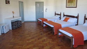 A hotel room with three wooden beds, a small desk with a chair, a refrigerator, and a door with a light switch. - Hotel Centenário (Juiz de Fora)