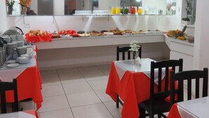 A buffet setup with various food items and beverages, tables with red tablecloths, and a mirror reflecting the room. - Hotel Centenário (Juiz de Fora)