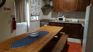 Een keuken met houten kastjes, een magnetron, een fornuis en een houten tafel met een kleed.