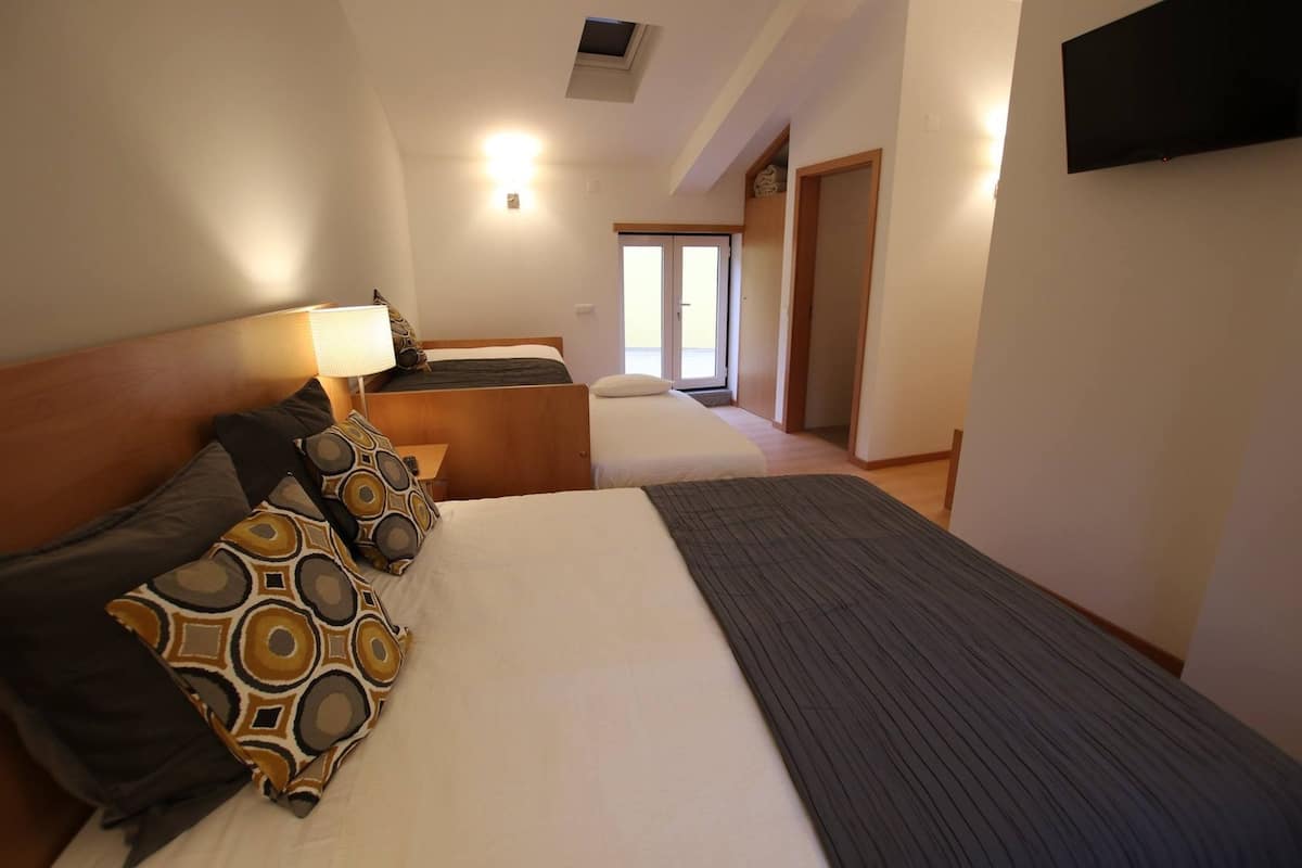 A hotel room with a large bed, a bedside table with a lamp, a TV mounted on the wall, and a sliding door leading to a balcony.