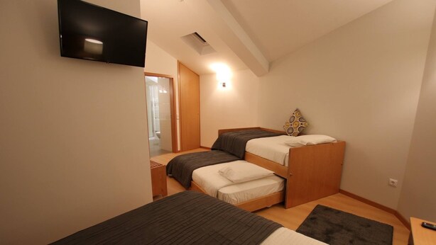 Een kleine, goed verlichte kamer met twee stapelbedden, een flatscreen televisie aan de muur en een houten deur die naar een andere kamer leidt.