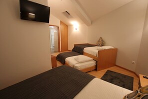Een kleine, goed verlichte kamer met twee stapelbedden, een flatscreen televisie aan de muur en een houten deur die naar een andere kamer leidt.