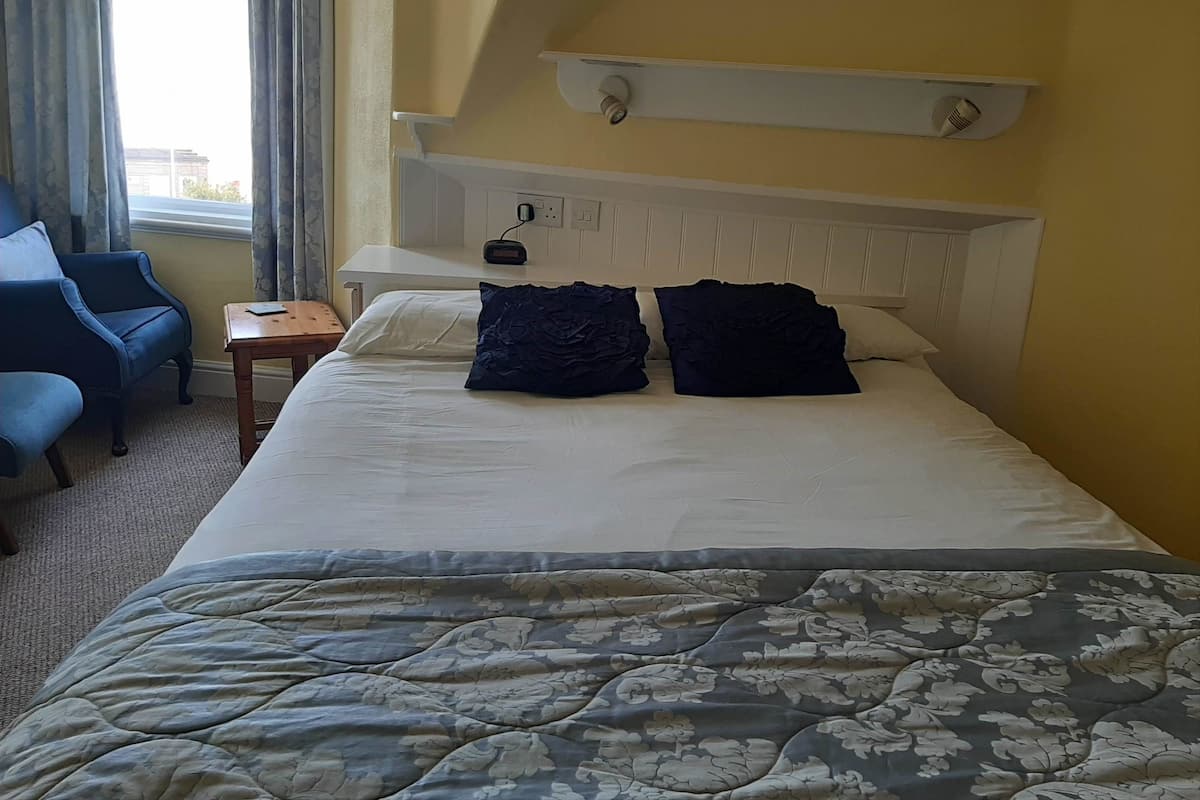 A hotel room with a bed, a chair, a nightstand, and a window with curtains.