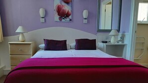 Una cama con cabecera blanca, dos almohadas, una manta roja y un cuadro de flores colgado en la pared.