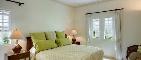 A bedroom with a bed, two nightstands, a ceiling fan, and windows with curtains.