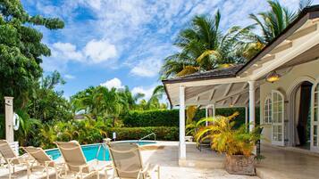 A pool area with lounge chairs, a covered patio, and palm trees.